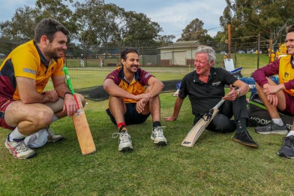 Four men sitting on the grass with cricket bats and talking