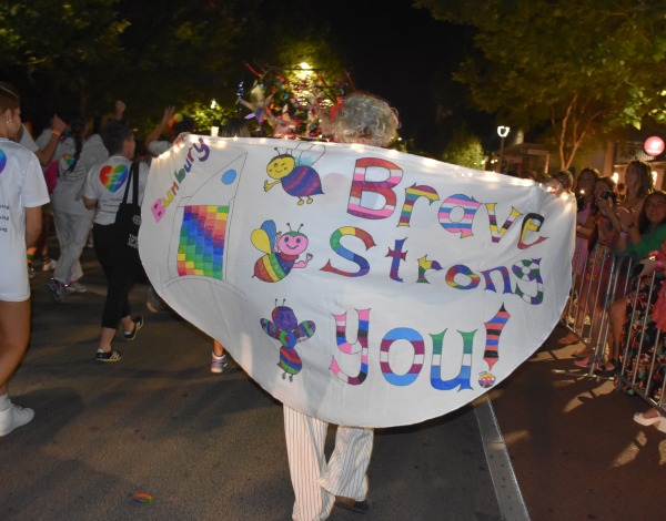 Someone holding a banner that says brave strong you, covered in various rainbow lgbtqia+ patterns