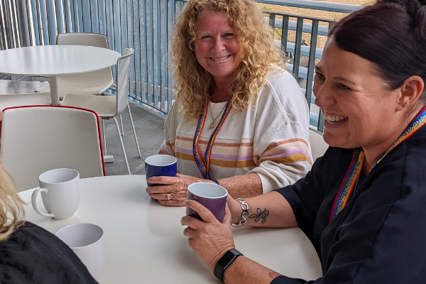 Two women sitting a white table, each smiling and holding cups