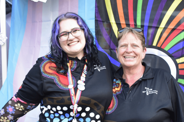 two people smiling in front of rainbow flags