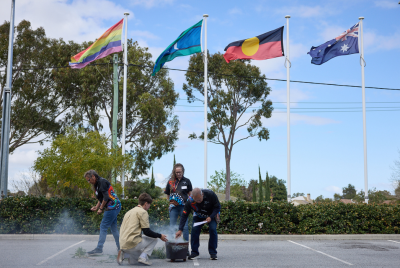 Four people crouching and setting something up in front of the australian, aboriginal, torres strait island, and lgbtqia plus pride rainbow flags