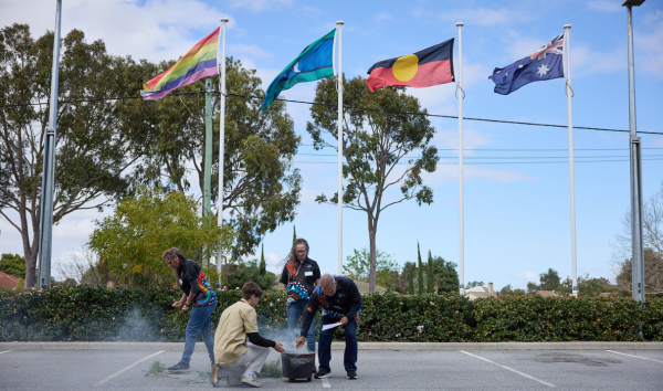 Four people crouching and setting something up in front of the australian, aboriginal, torres strait island, and lgbtqia plus pride rainbow flags