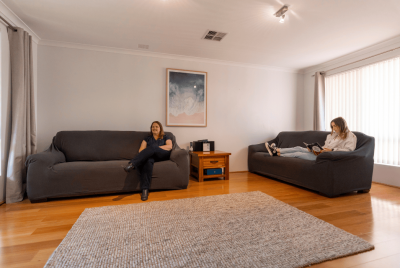 Two women sitting on darkly coloured couches in a room with a big grey rug and a painting in the background