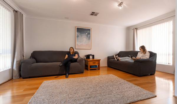 Two women sitting on darkly coloured couches in a room with a big grey rug and a painting in the background