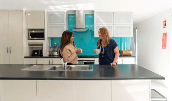two people in a kitchen talking with coffee mugs