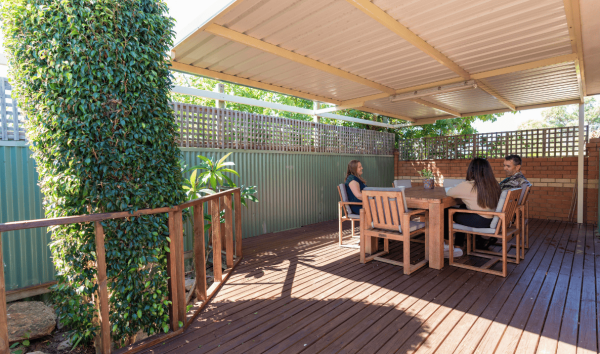Three people sitting outside on a wooden table on a wooden deck