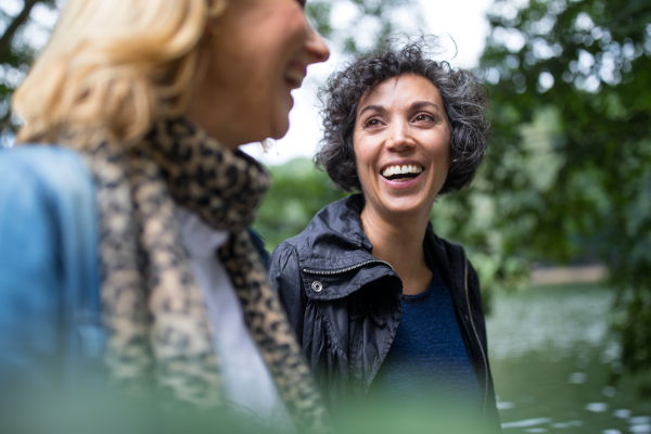Two women smiling at one another while standing around trees