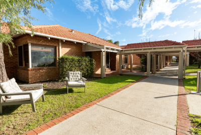 The walkway leading up to an orange brick house with two chair on the grass out front