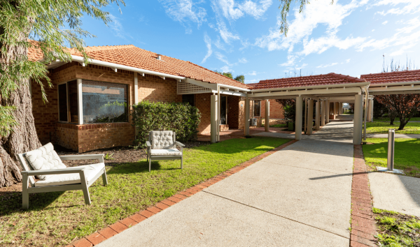 The walkway leading up to an orange brick house with two chair on the grass out front