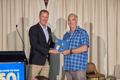 A man in a suit presenting a man with a blue flannel shirt with an award on a stage