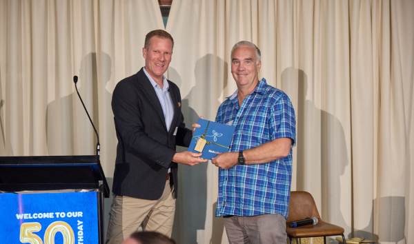 A man in a suit presenting a man with a blue flannel shirt with an award on a stage