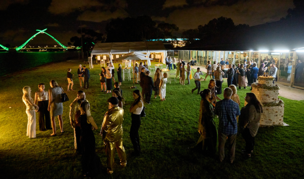 A group of people at an event at night on the grass in front of some buildings