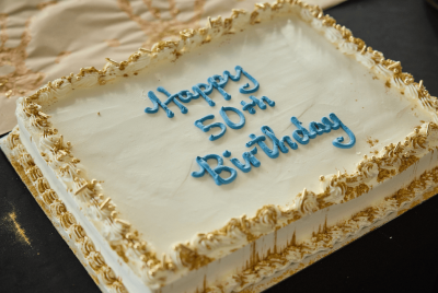 A white birthday cake that says Happy 50th Birthday in blue icing