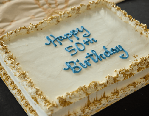 A white birthday cake that says Happy 50th Birthday in blue icing