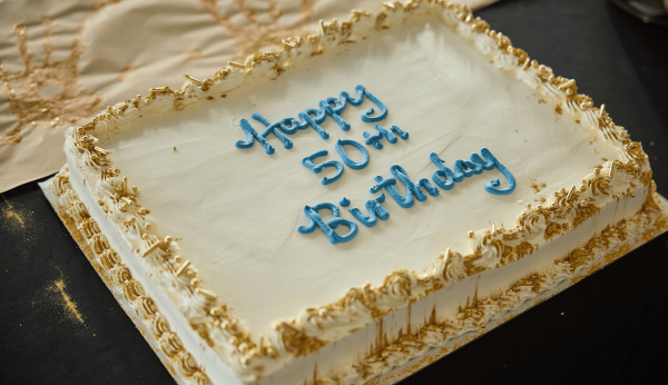 A white birthday cake that says Happy 50th Birthday in blue icing