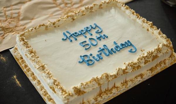 A white birthday cake that says Happy 50th Birthday in blue icing