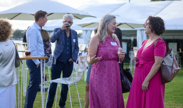 Two women speaking at at event on the grass while two men drink from cups in the background