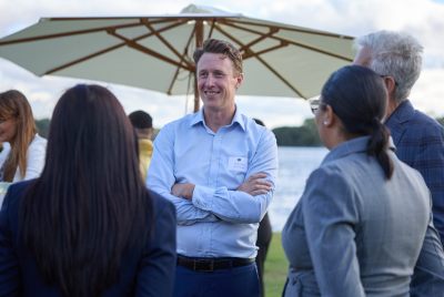 Four people standing in a circle and talking at an event on the grass in front of the river
