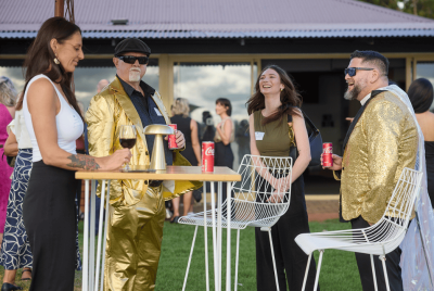 Two men in gold suits standing around a table with two women and talking at an event