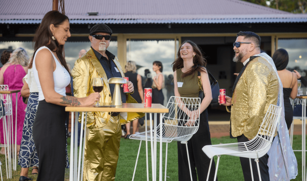 Two men in gold suits standing around a table with two women and talking at an event