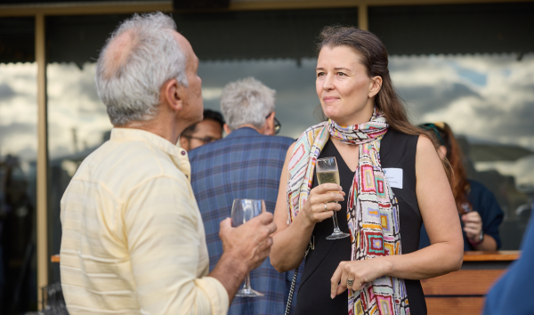 A woman in a colourful scarf holding a drink and speaking with a man who is also holding a drink