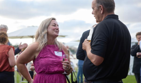 A woman in a pink dress holding a drink and talking to a man in a black shirt at an event