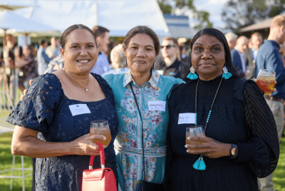 Three woman standing together and holding drinks while looking into the camera at an event