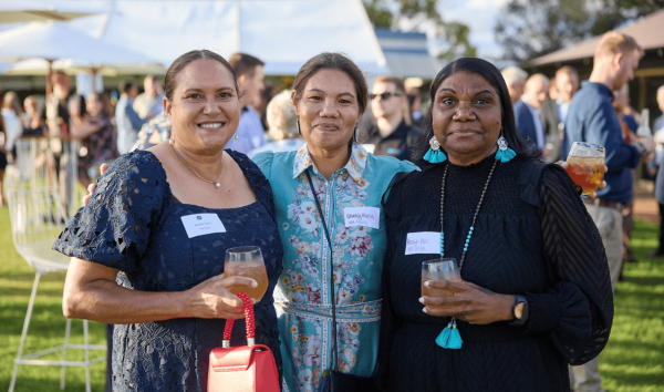 Three woman standing together and holding drinks while looking into the camera at an event