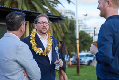 Three men in suits holding drinks while talking at an event while one of them wears a gold necklace