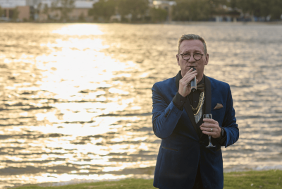 A man in a blue suit giving a speech into a microphone while standing in front of the river