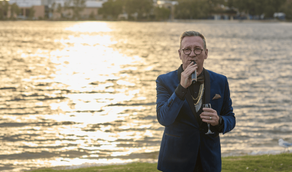A man in a blue suit giving a speech into a microphone while standing in front of the river