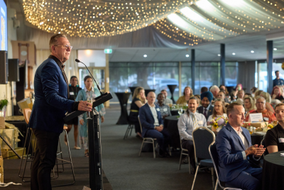 A man in a blue suit standing on a stage and giving a speech into a microphone to a group of people at an event