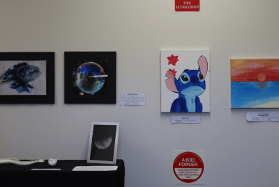 A white wall with various decorations including a picture of Stitch from the Disney movie, a picture of a sunset, an image of the moon and an image of a bubble