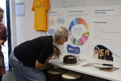 A woman in a black shirt bending forward to a grab a piece of cake that is sitting in front of a Richmind WA display