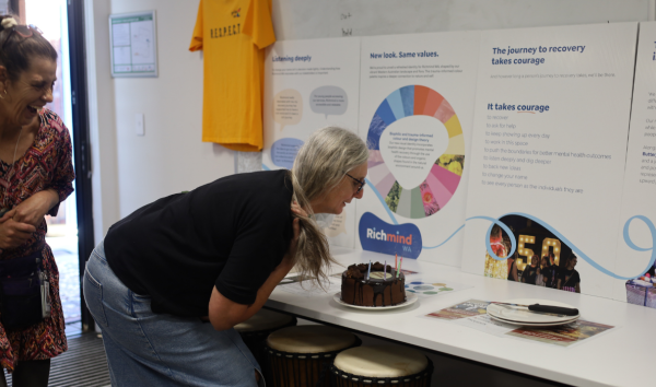 A woman in a black shirt bending forward to a grab a piece of cake that is sitting in front of a Richmind WA display