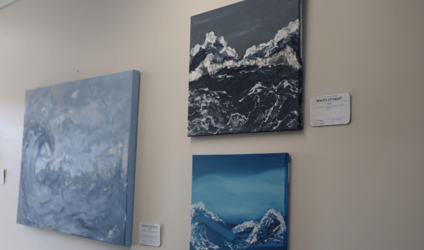 Three blue paintings of the ocean displayed on a white wall