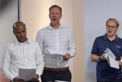 Three men singing while reading from sheets of paper
