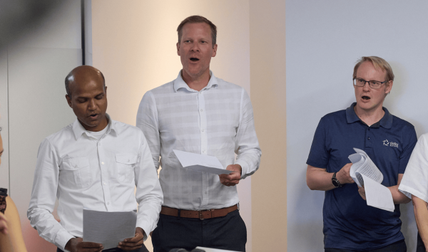 Three men singing while reading from sheets of paper