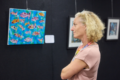A woman crossing her arms and looking at a blue painting with orange and pink fish