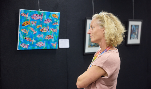 A woman crossing her arms and looking at a blue painting with orange and pink fish