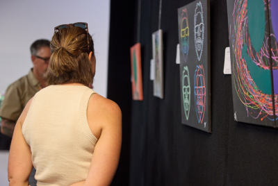 A woman and a man looking at various colourful pieces of art at an exhibition