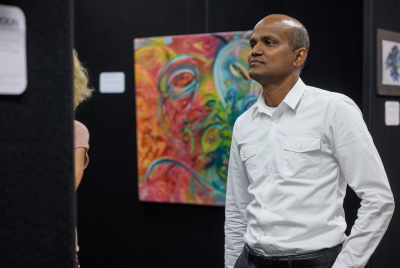 A man in a collared shirt at an exhibition with a colourful piece of art in the background