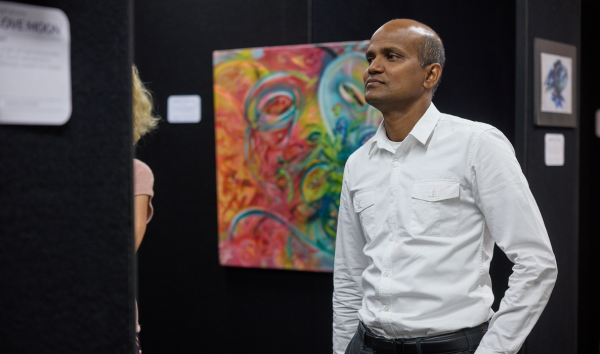 A man in a collared shirt at an exhibition with a colourful piece of art in the background