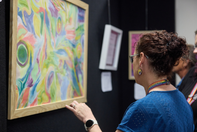 A woman in a blue shirt looking at a piece of multicoloured art at an exhibition