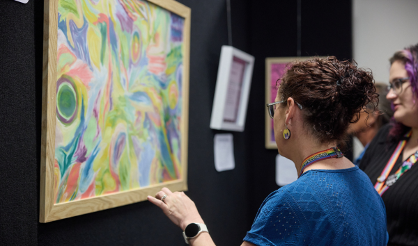 A woman in a blue shirt looking at a piece of multicoloured art at an exhibition