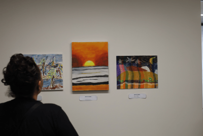 A woman looking at three pieces of aboriginal art depicting sunset, the night sky and one more thing