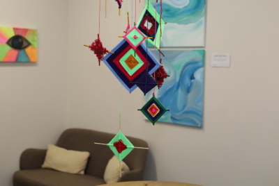 A display at an exhibit with paintings in the background a series of multicoloured squares hanging from the ceiling