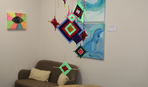 A display at an exhibit with paintings in the background a series of multicoloured squares hanging from the ceiling