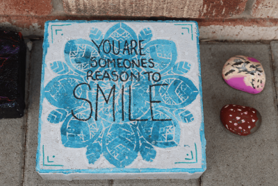 A blue and white stone cube with the you are someone's reason to smile written on it in black icing