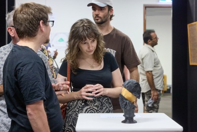 A woman examining a sculpture at an exhibition while other people look around